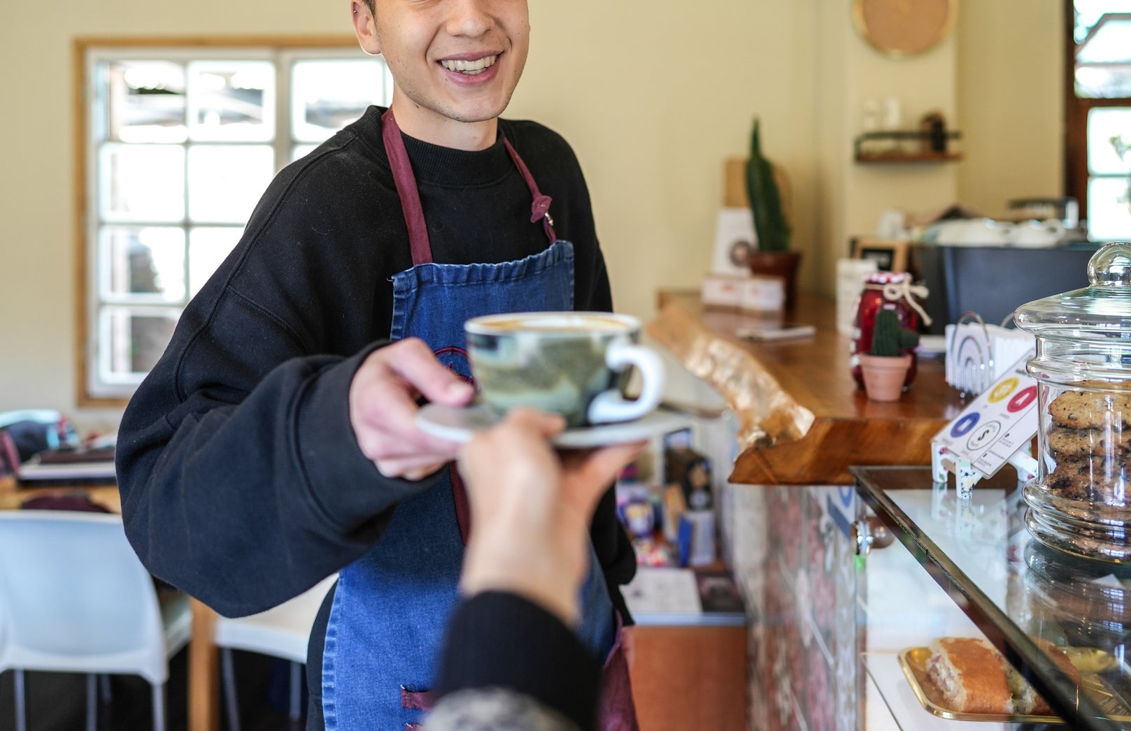 A young barista serves a drink to a customer at a cozy café, smiling warmly