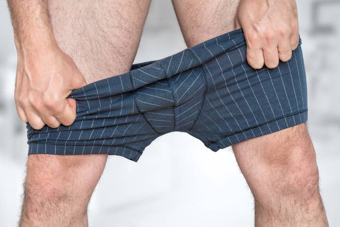 A person pulling at the waistband of their striped boxer shorts, showing only their torso and legs