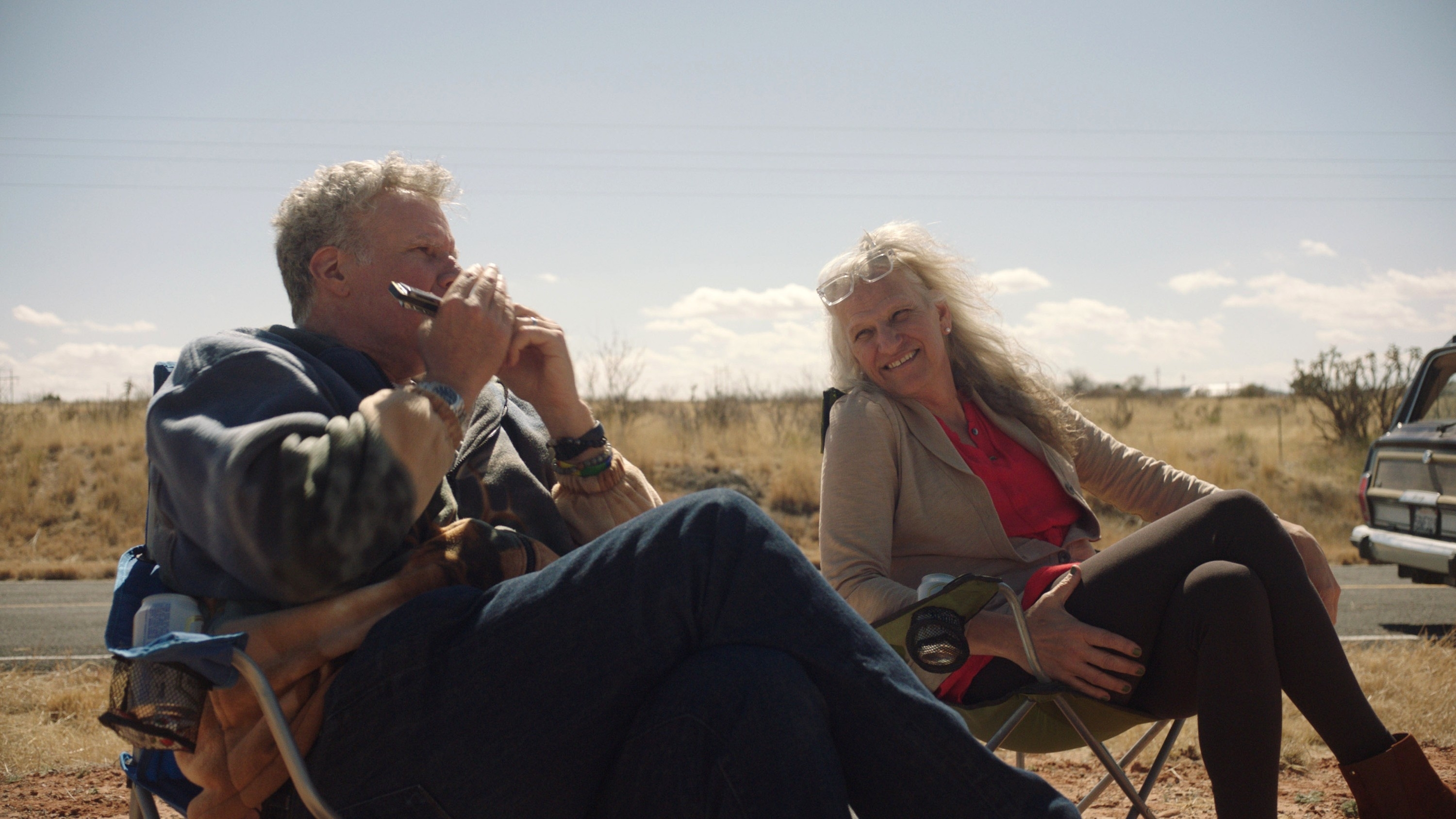 Will Ferrell and Harper Steele sit in outdoor chairs, smiling and talking in a rural setting