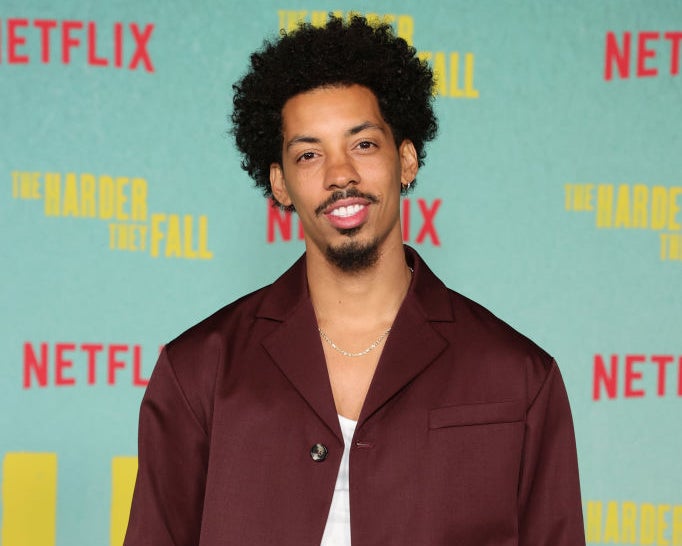 Melvin Gregg smiles, wearing a dark suit and white shirt, at "The Harder They Fall" Netflix premiere event
