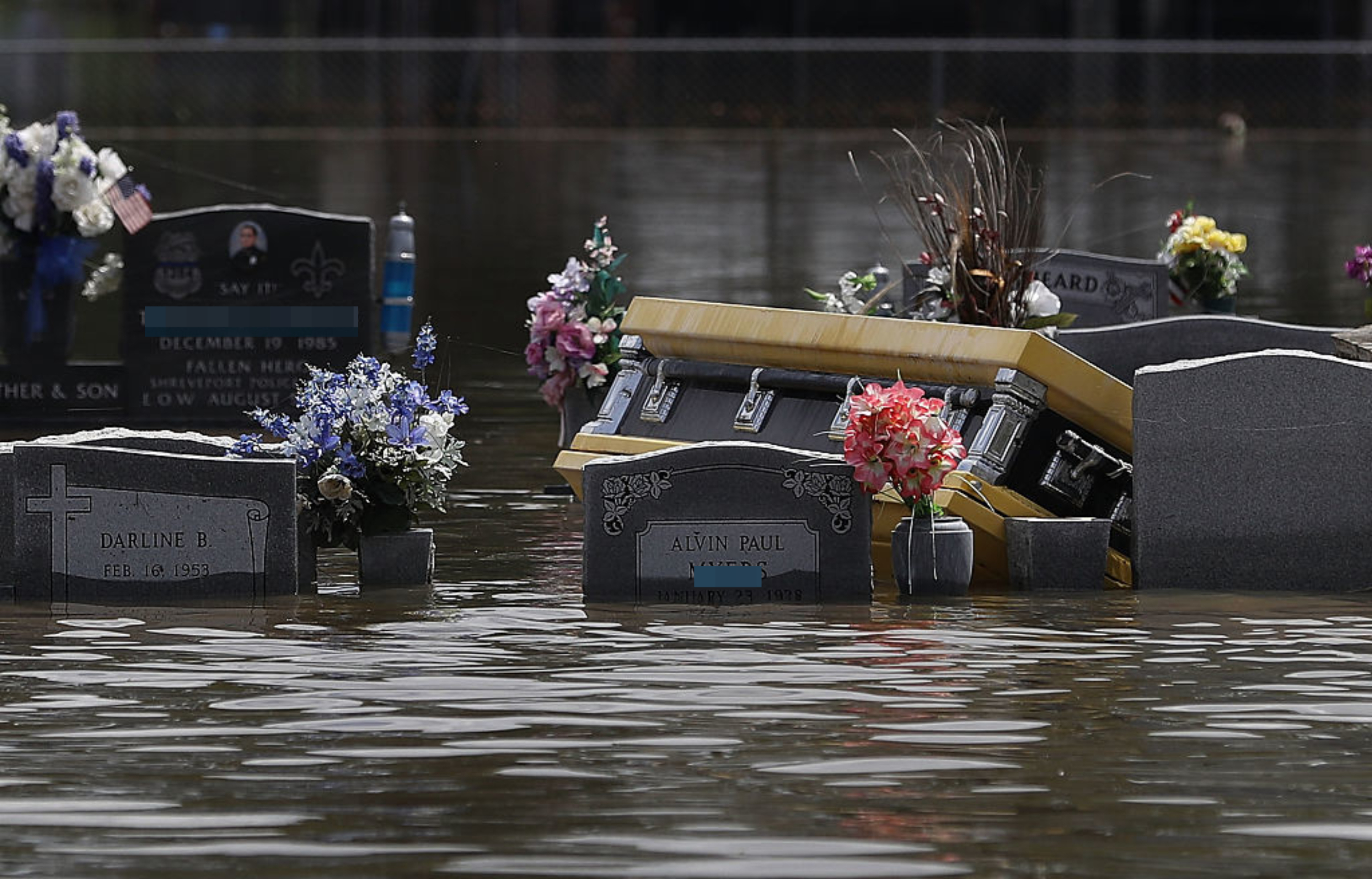 Flooded cemetery with partially submerged headstones and a floating casket are visible in the image