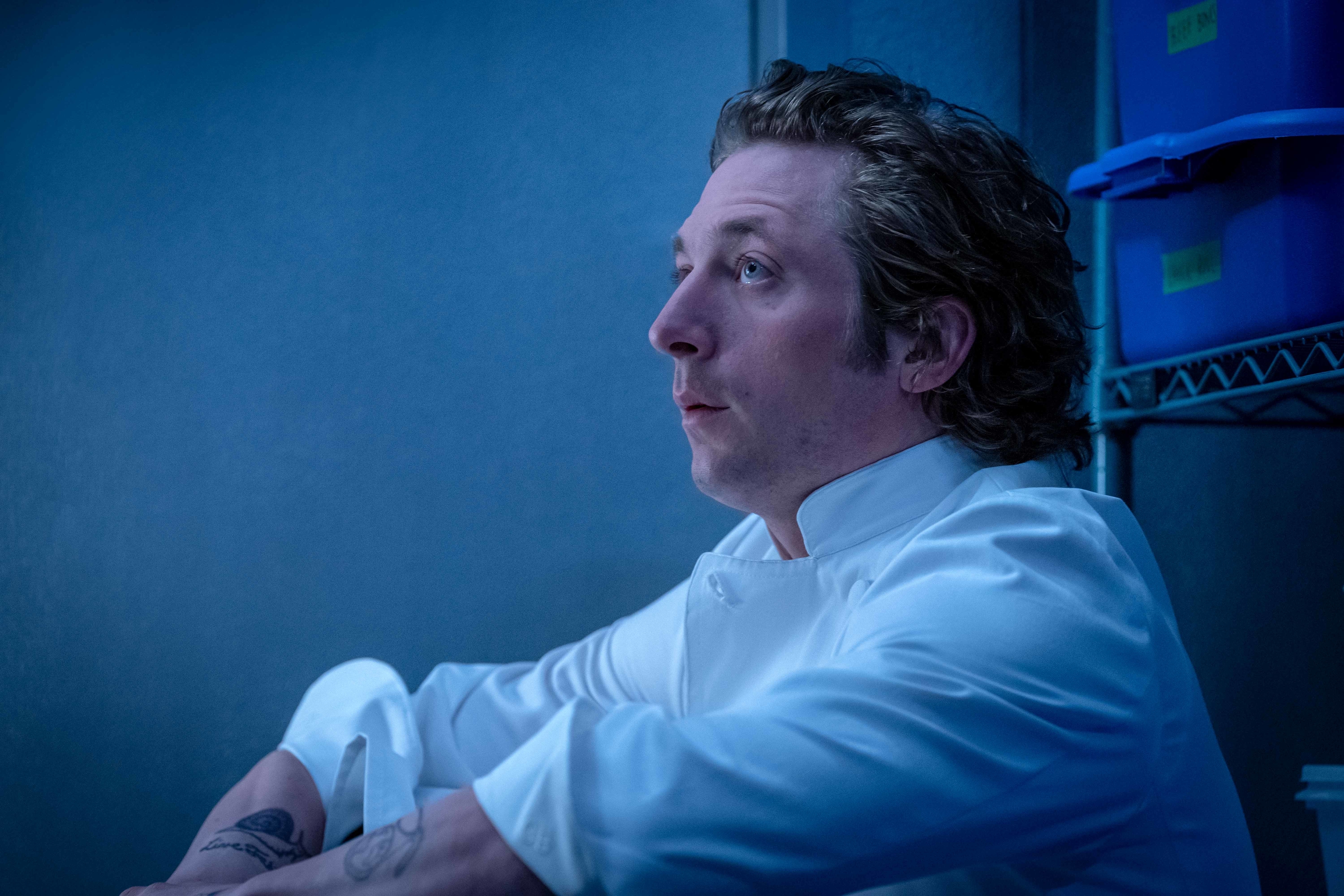 Jeremy Allen White in a scene from &quot;The Bear,&quot; dressed in a chef's white uniform, sitting in a storage area with shelves and containers in the background