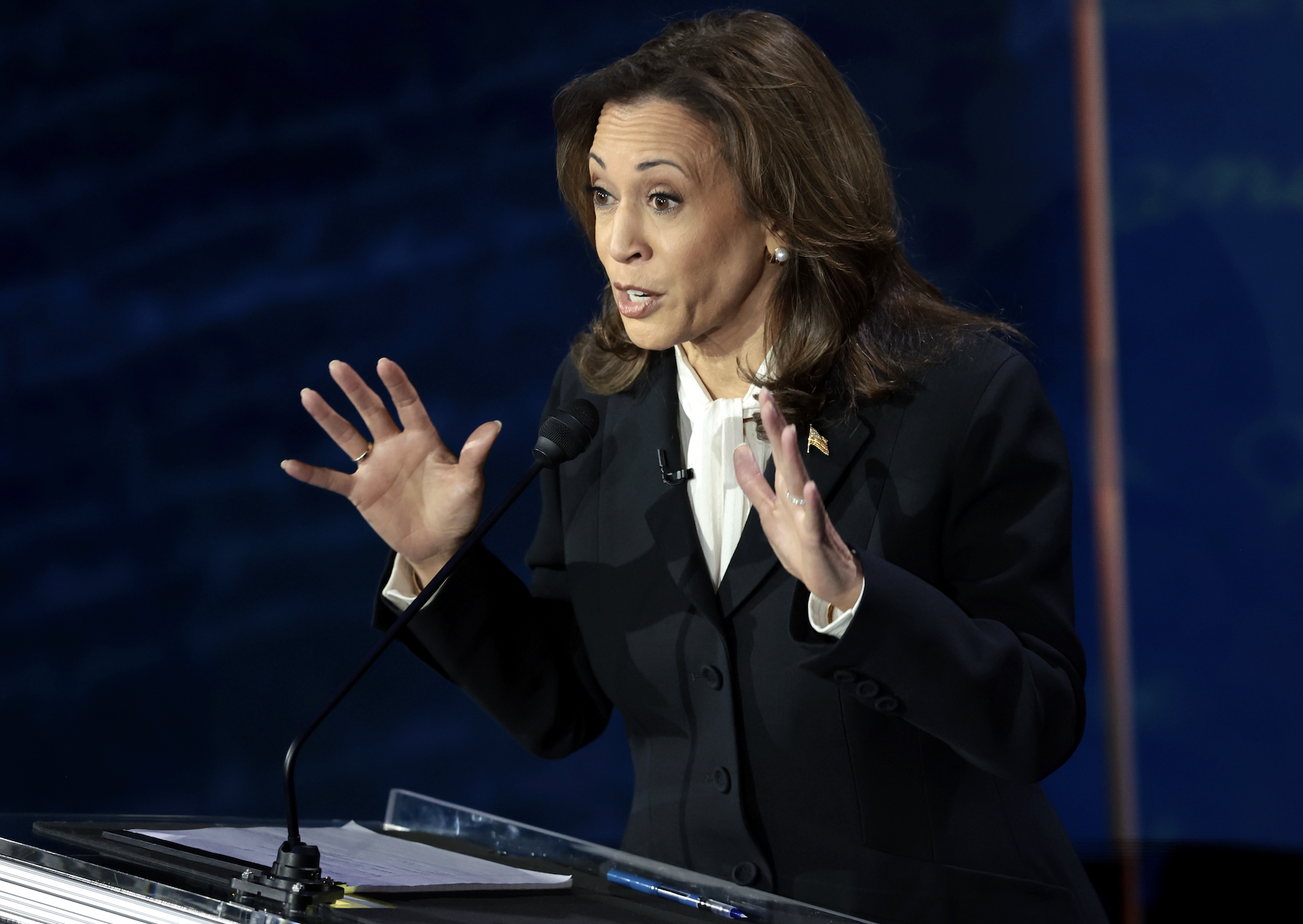 Kamala Harris speaks passionately behind a podium during a public event, gesturing with both hands