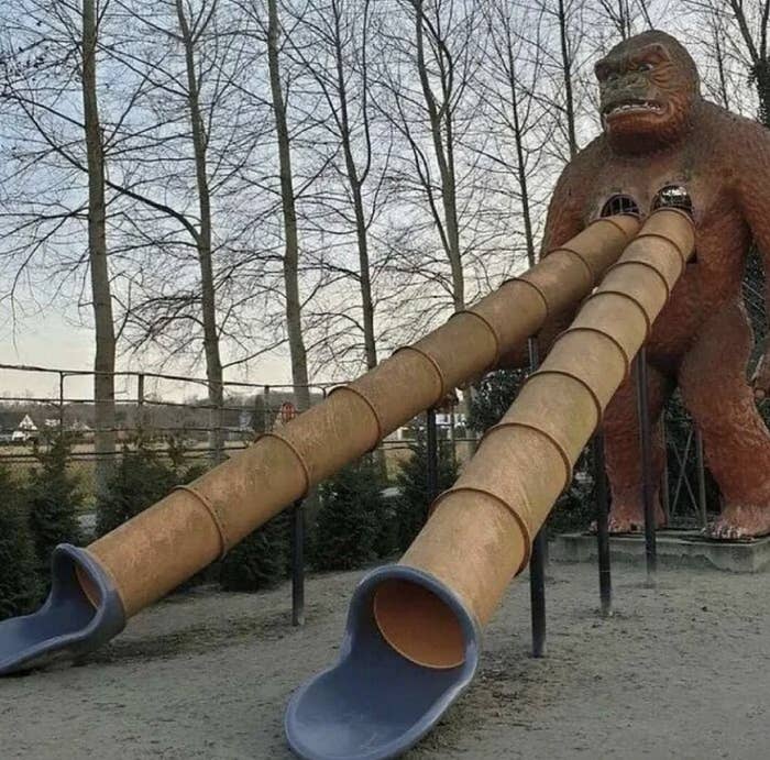 A large playground slide shaped like a gorilla with two long tube slides emerging from its chest. Trees are in the background