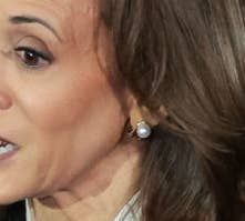 Kamala Harris gestures while speaking at an event. She wears a black suit with a white shirt