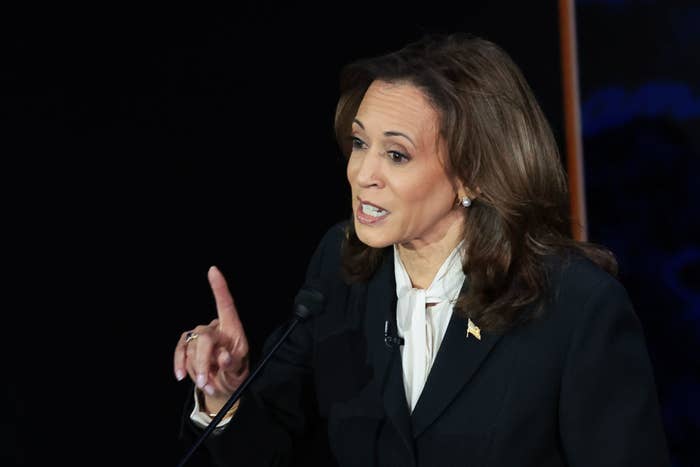 Kamala Harris gestures while speaking at an event. She wears a black suit with a white shirt