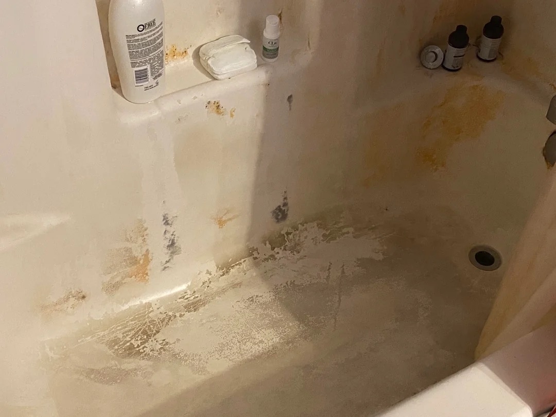 A dirty bathtub with soap scum, rust stains, and various personal care products on the ledges