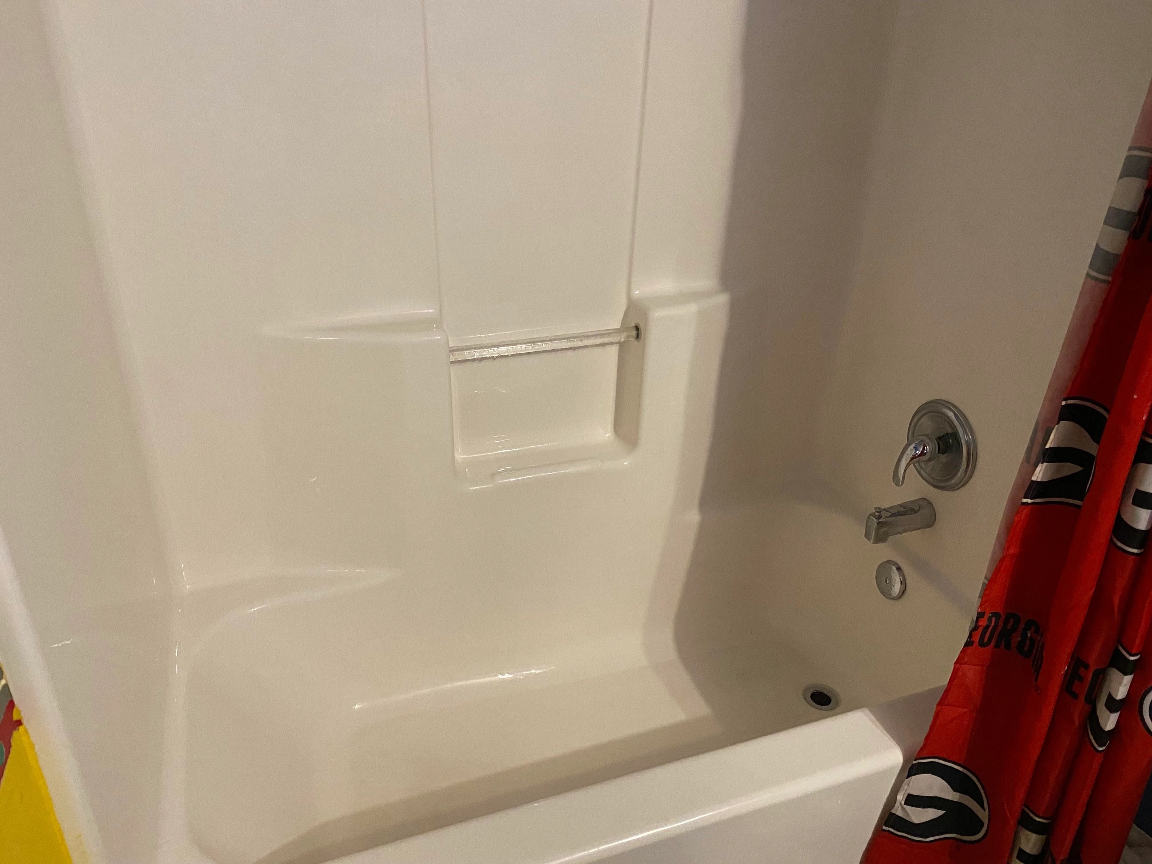 White bathtub and shower unit with a small built-in ledge, silver faucet, and red curtain partially visible on the right