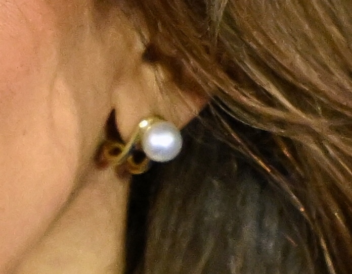 Close-up of an earlobe wearing a single pearl stud earring attached to a gold loop