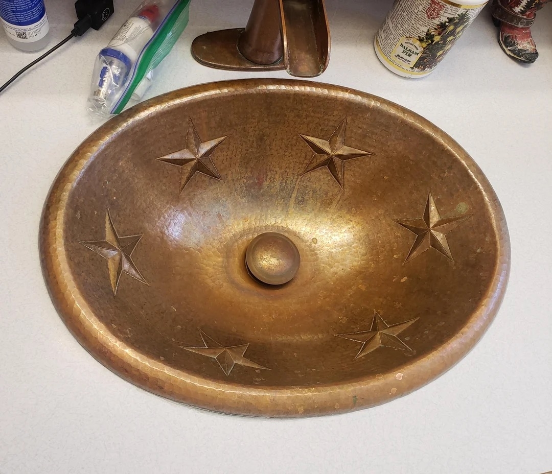 A copper sink with embossed star designs is installed on a countertop surrounded by various bathroom items