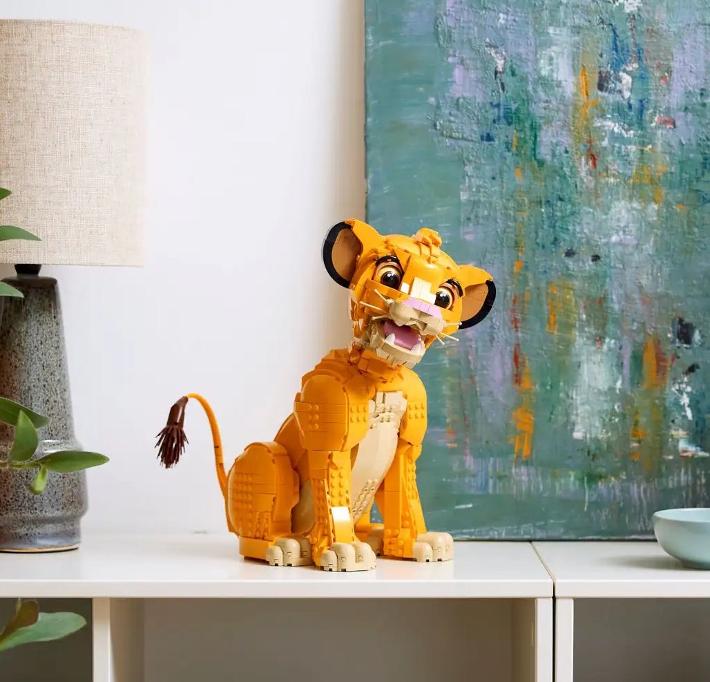 Bookshelf topped with potted plants, a lamp, and a detailed figurine of Simba from The Lion King; an abstract painting hangs on the wall behind it
