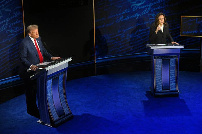 Donald Trump and Kamala Harris debate on stage, both standing at blue podiums. Kamala gestures while speaking