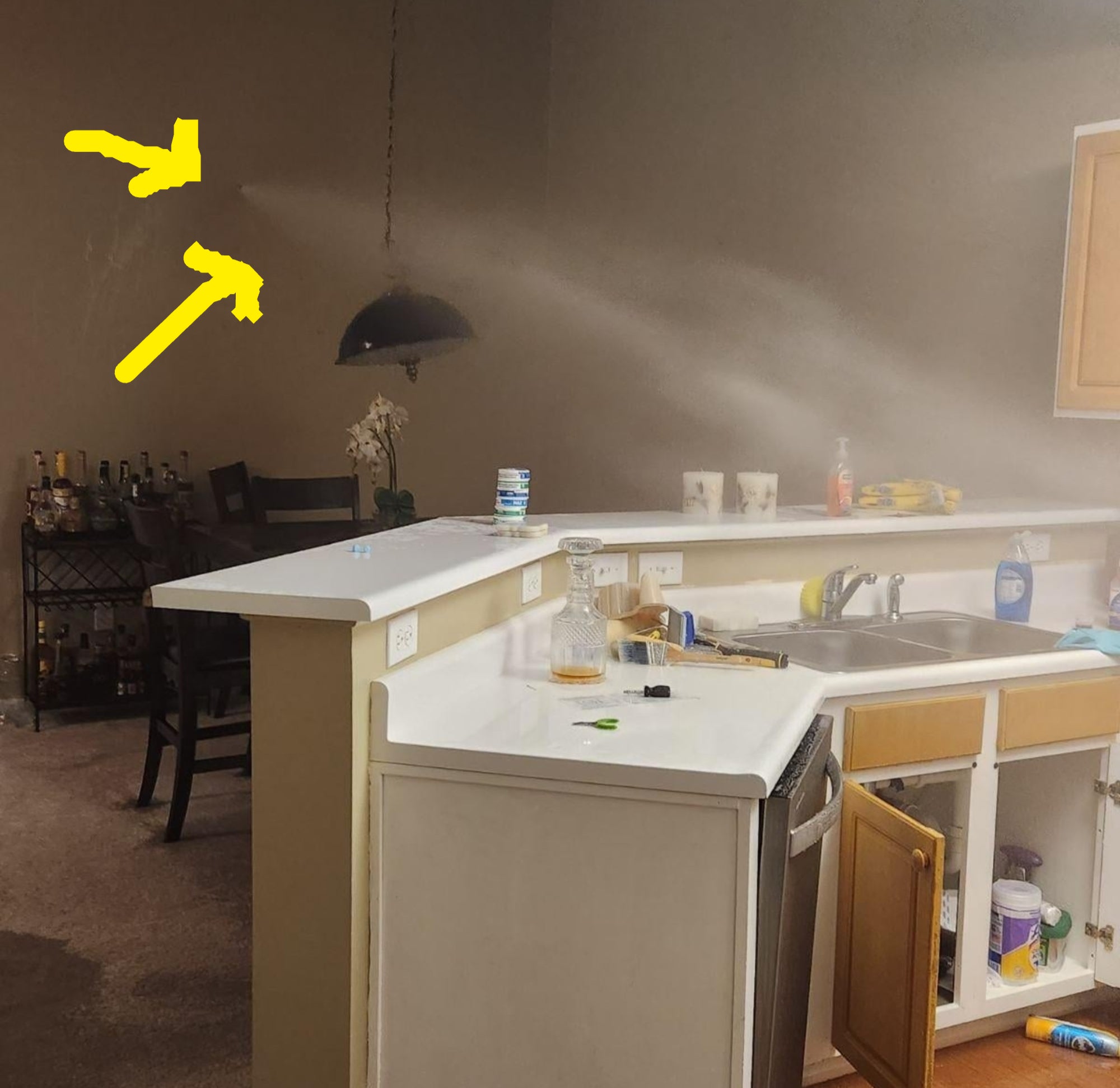 Water sprays from a broken kitchen sink pipe in a home, causing flooding near an open cabinet and countertop appliances