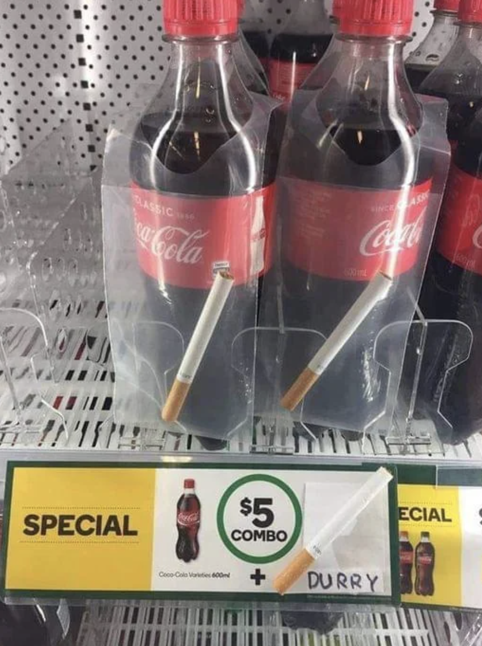 Two Coca-Cola bottles with a cigarette in each plastic packaging. A sign advertises a $5 combo for the cola and cigarettes