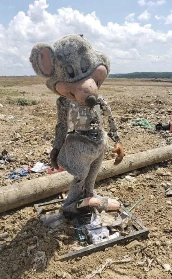 A deteriorated Chuck E. Cheese mascot standing in a desolate, trash-strewn area, revealing structural damage and mechanical parts