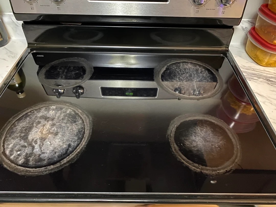 A four-burner electric stovetop with residue on three burners and clean countertops on the sides