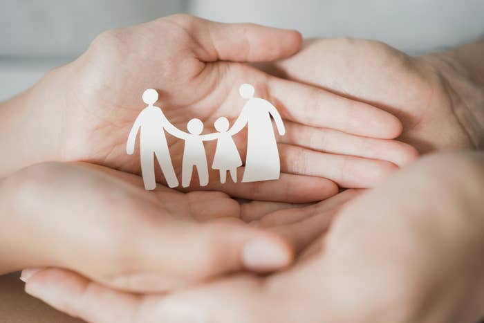 Hands cradling a paper cut-out depicting a family of four holding hands, highlighting the concept of family unity and care