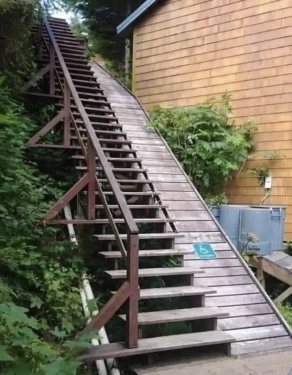 An outdoor staircase with a wooden ramp alongside it. There is a sign indicating the ramp is for wheelchair access
