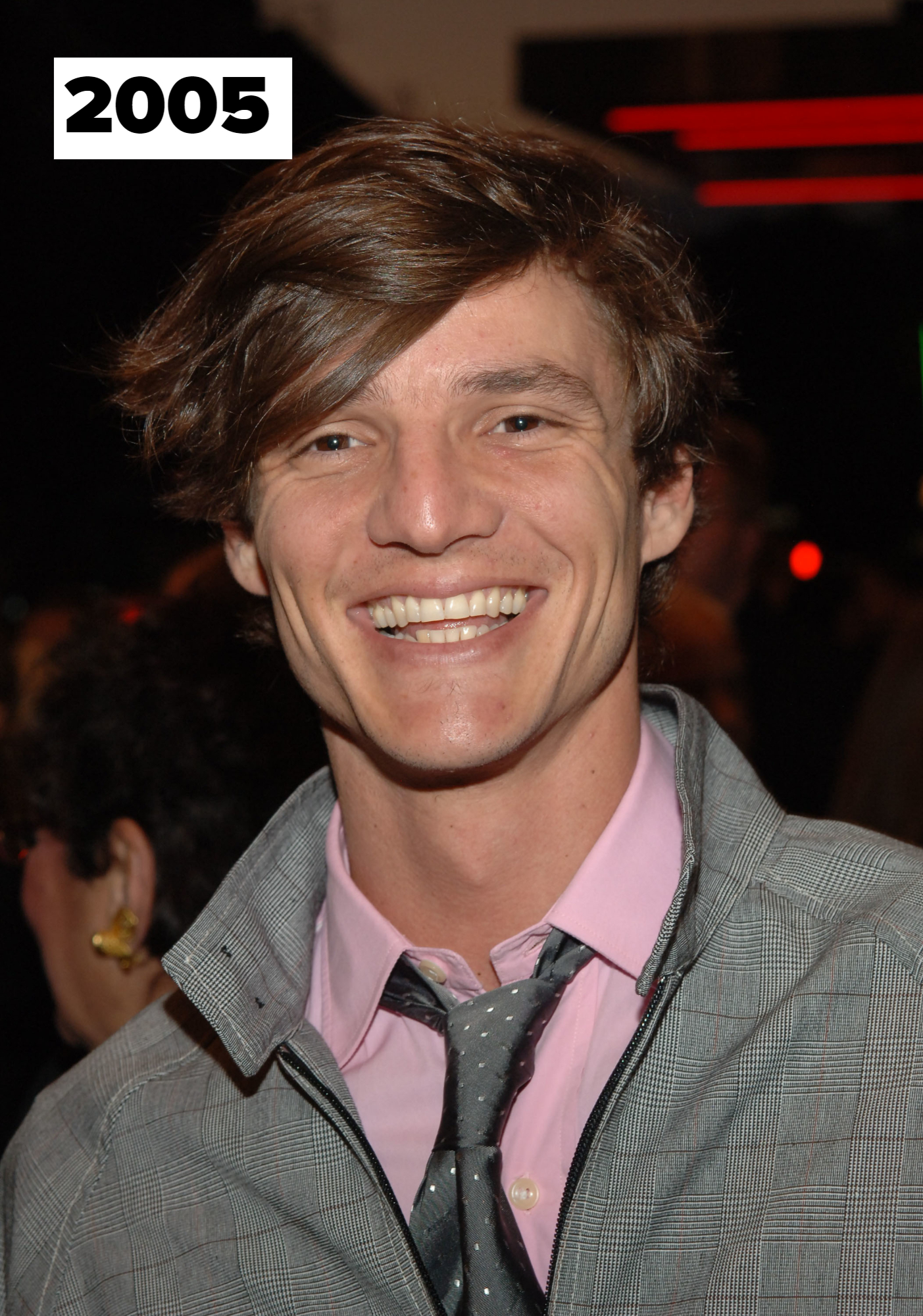 Pedro Pascal smiling at an event, wearing a checkered jacket over a pink shirt and dotted tie
