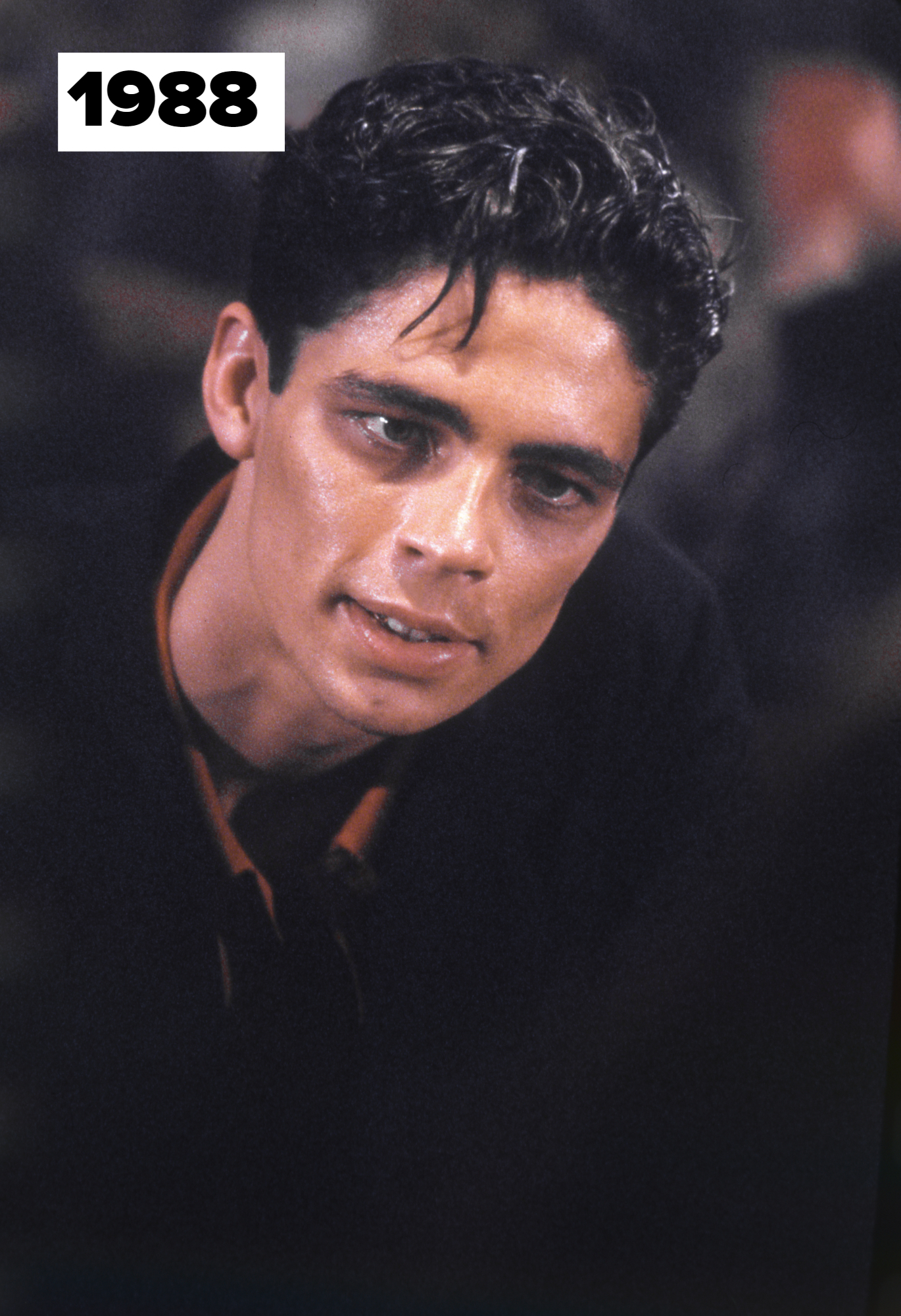 Benicio Del Toro with wet, slicked-back hair and intense expression wearing a dark, collared shirt