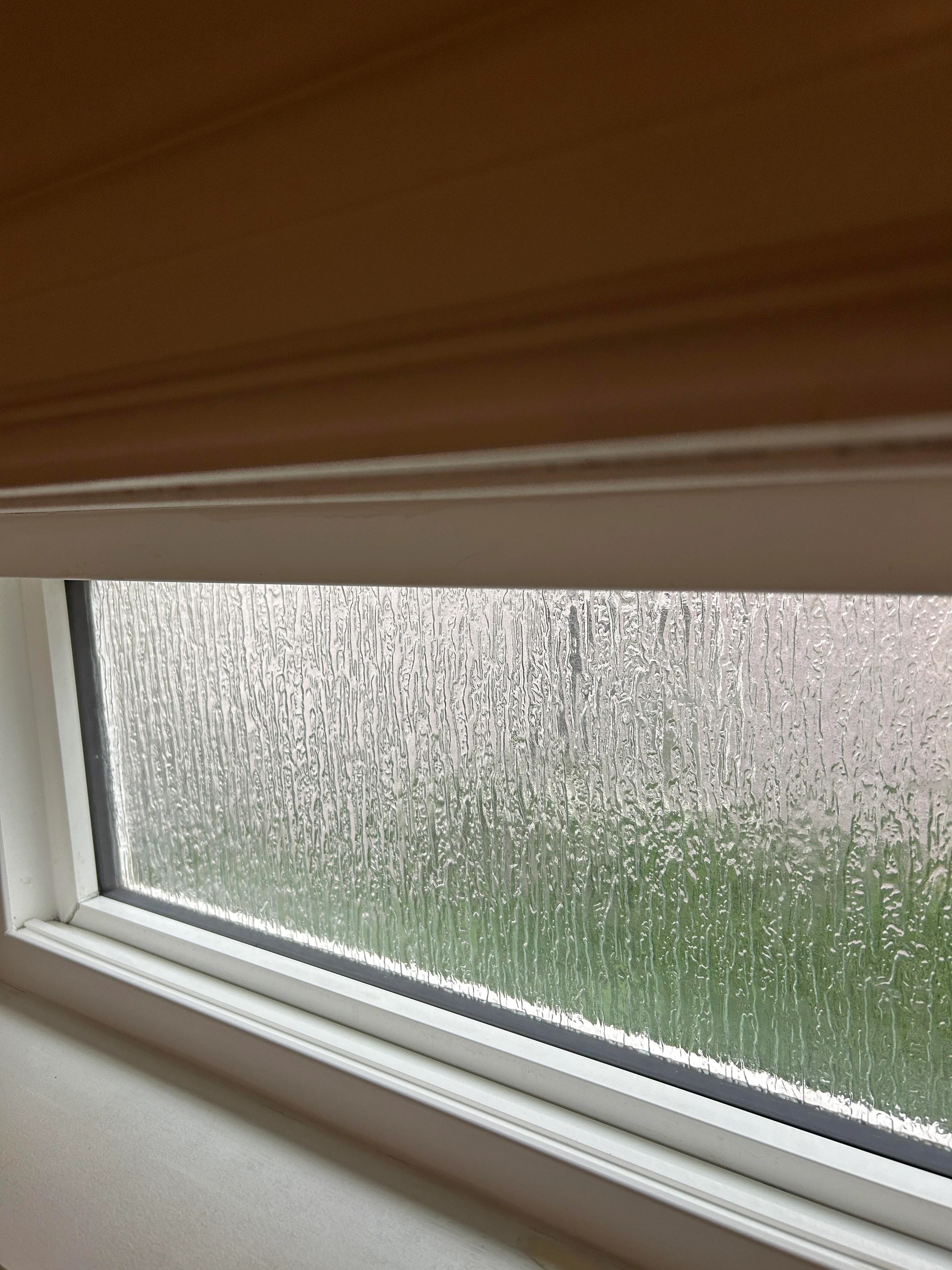 Rain drops streaked down a windowpane, with a blurred view of grass and outdoors visible through the glass