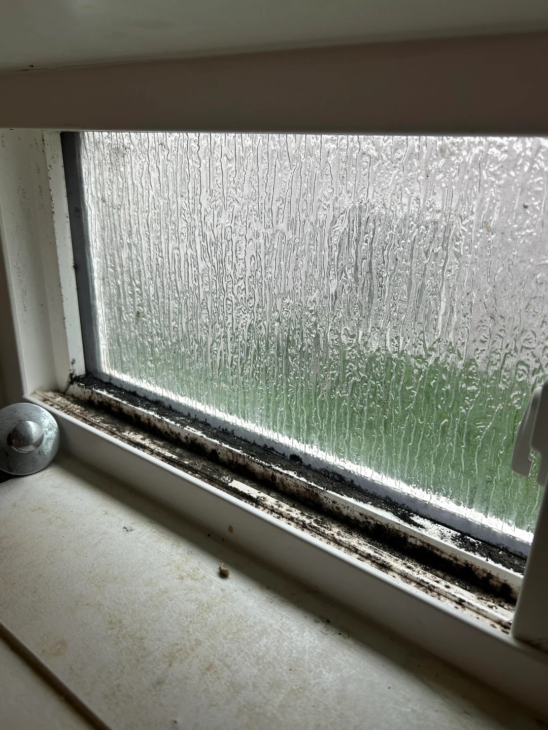 A close-up view of a dirty and moldy window sill with a frosted glass window