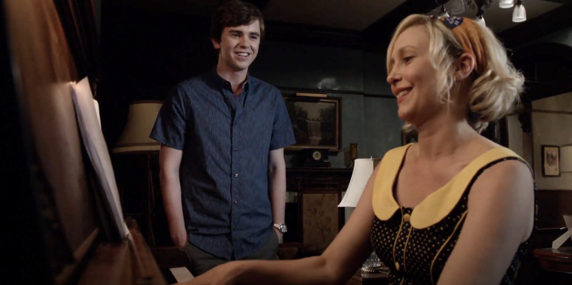 Freddie Highmore in a casual shirt watches Vera Farmiga playing the piano in a scene from a TV show or movie