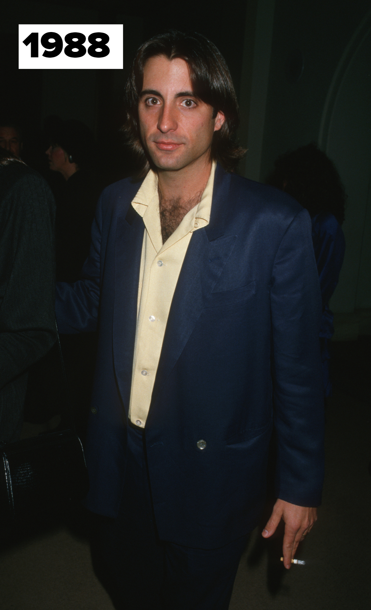 Andy Garcia in 1988, wearing a casual suit jacket over an open-collared shirt, with others visible in the background