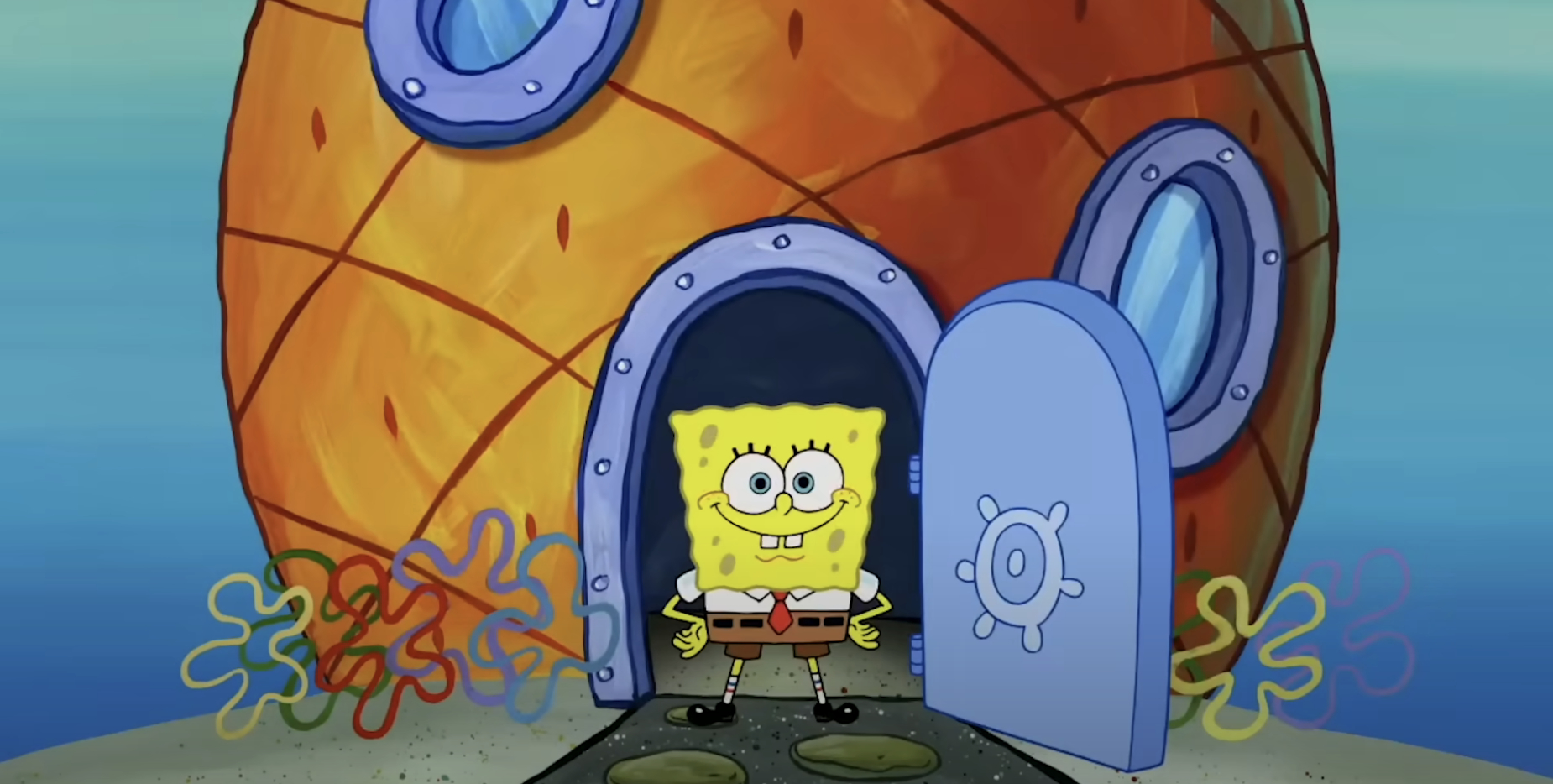 SpongeBob SquarePants stands smiling at the open door of his pineapple house