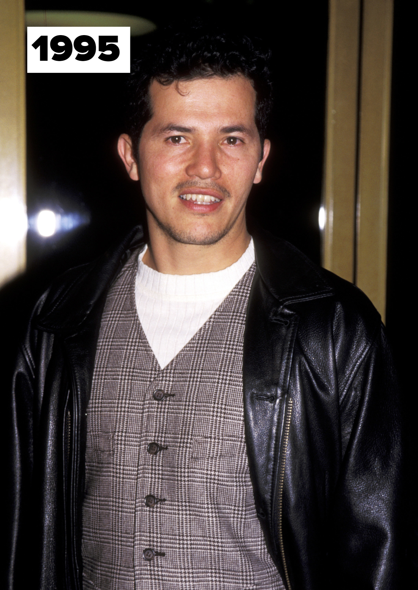 John Leguizamo in 1995, wearing a plaid vest over a white shirt with a black leather jacket