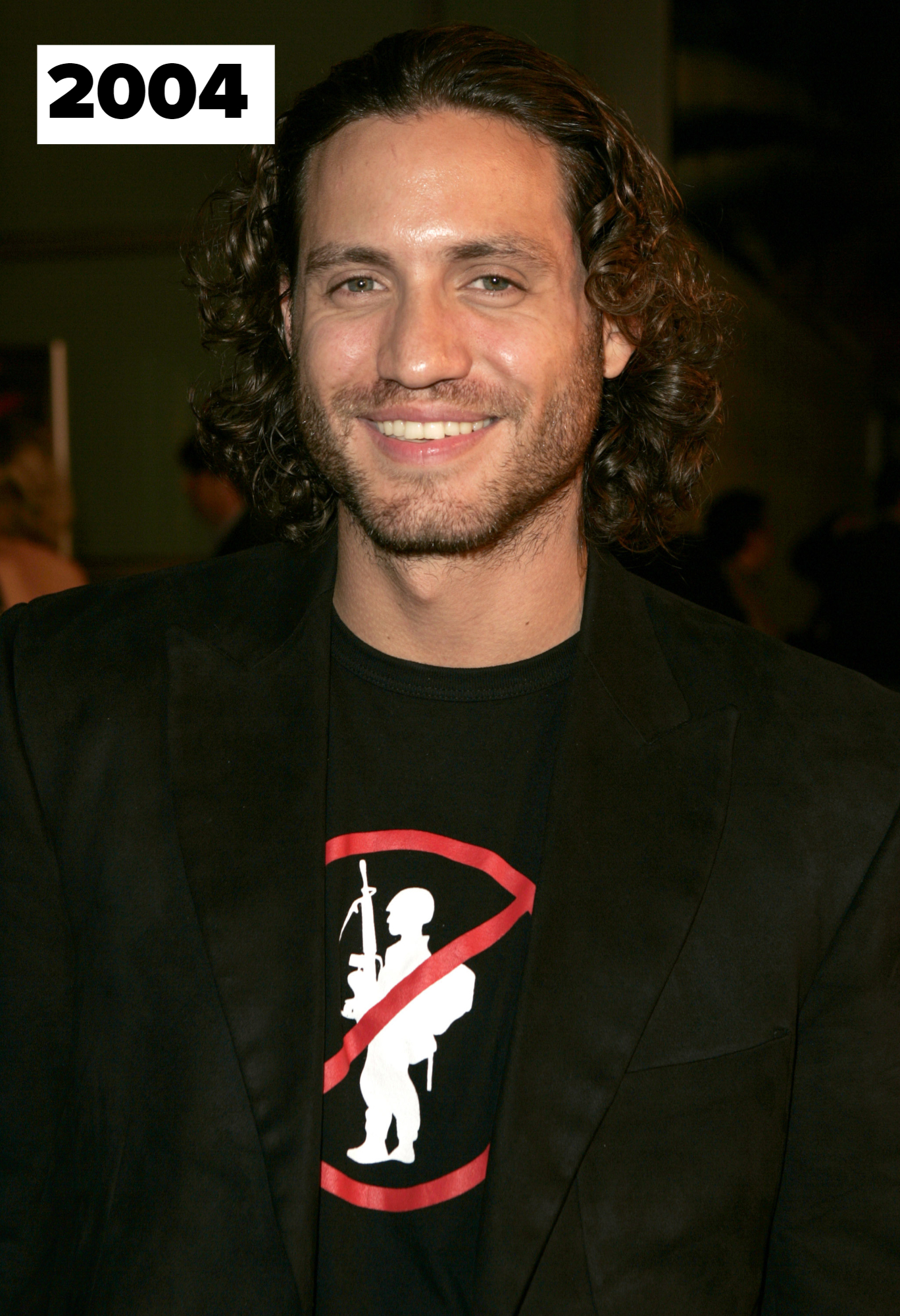 Edgar Ramirez in casual attire with a blazer and graphic tee smiles at an event.