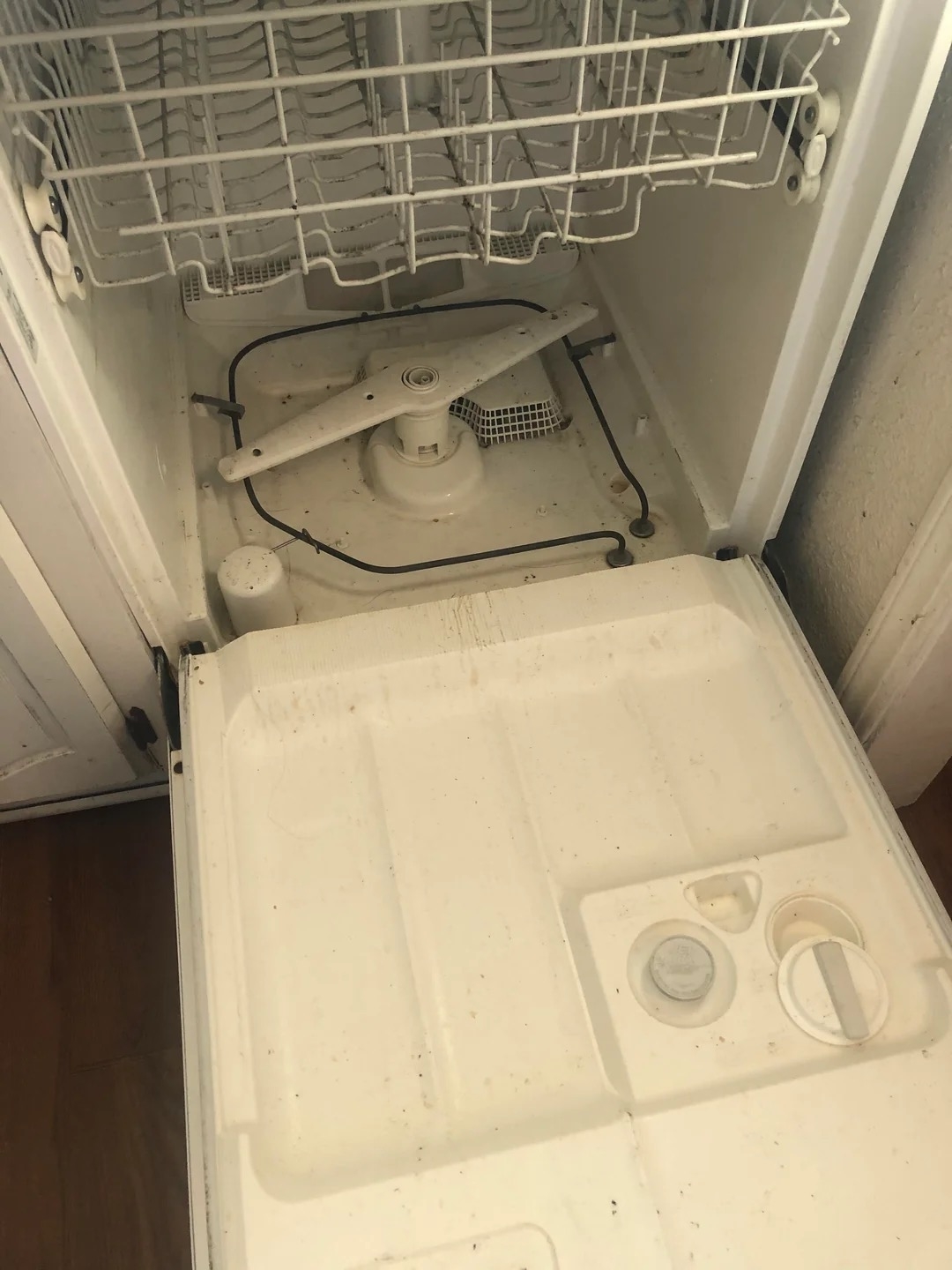 Open dishwasher with the bottom rack removed, showing the internal components and base.