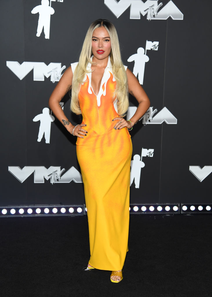 Karol G on the red carpet at the VMAs, wearing a long, fitted dress with a unique flame-like design