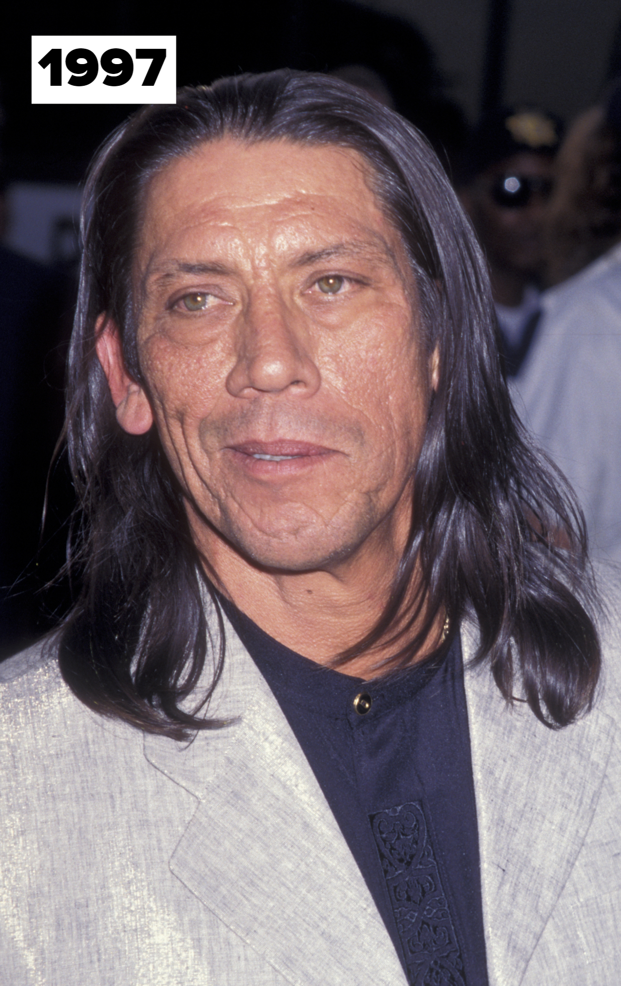 Danny Trejo at an event, wearing a light-colored blazer over a black shirt with intricate embroidery