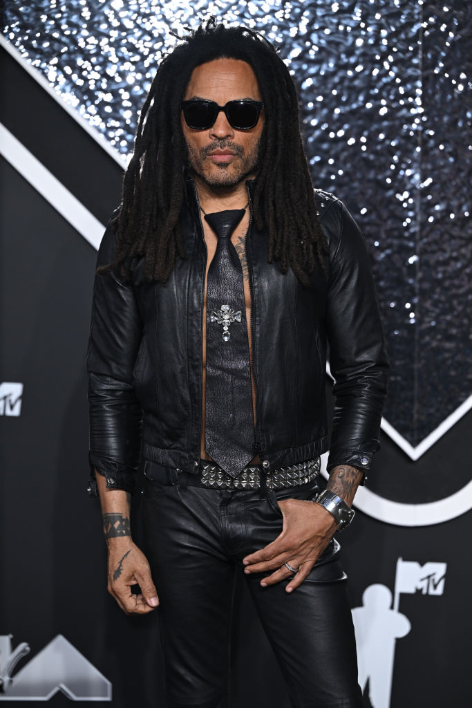 Lenny Kravitz at an event in a leather jacket with a cross necklace, leather pants, and sunglasses