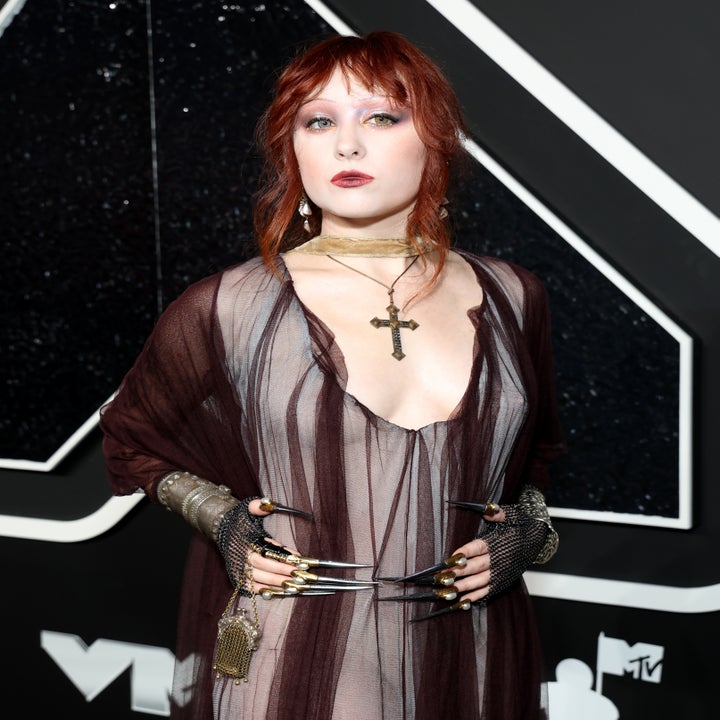 Actress Liv Hewson on the red carpet at the MTV VMAs, wearing a sheer dress with long black gloves and a large cross necklace