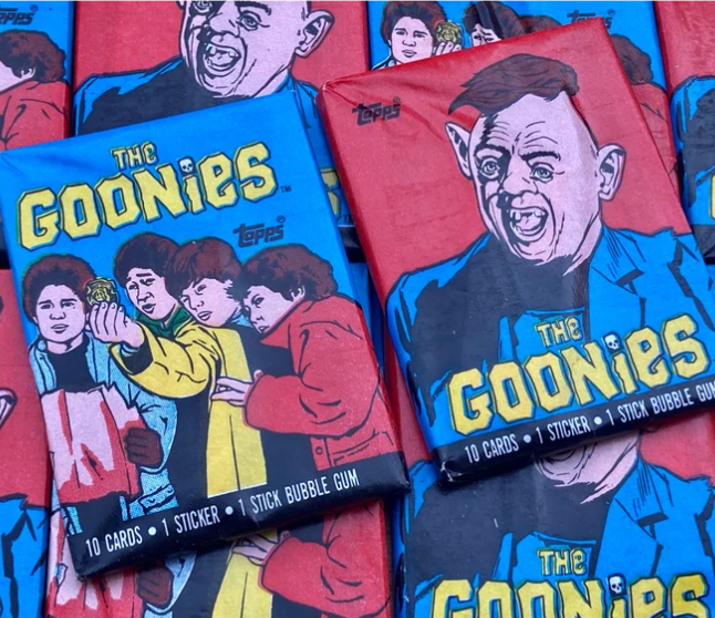 Two packs of vintage "The Goonies" trading cards by Topps, featuring artwork of characters from the movie "The Goonies". Text on the packs reads "10 cards, 1 sticker, 1 stick bubble gum"