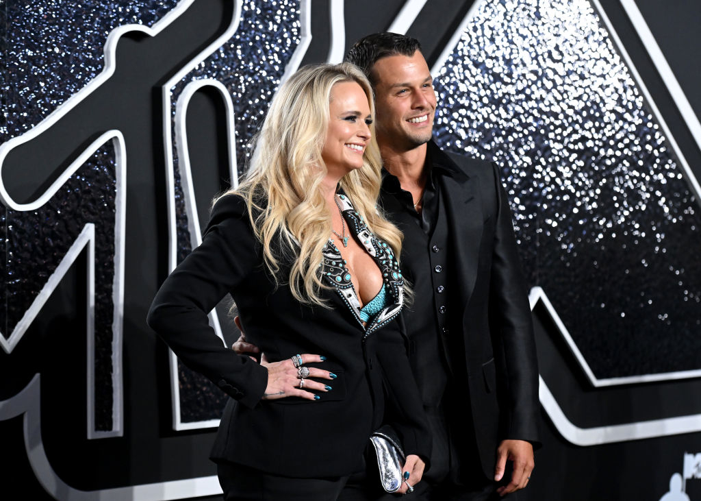 Miranda Lambert and Brendan McLoughlin pose together on the red carpet. Lambert is wearing a stylish outfit with turquoise accents, and he's in a collared shirt