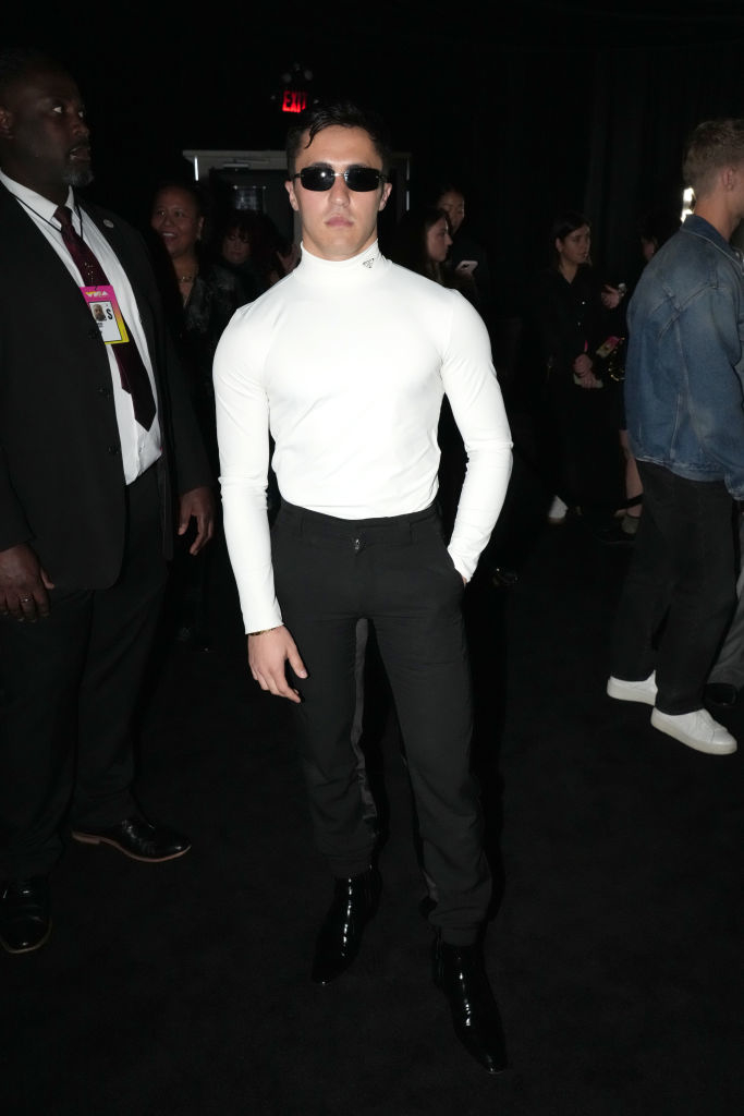 Chris is wearing a fitted turtleneck and dark pants