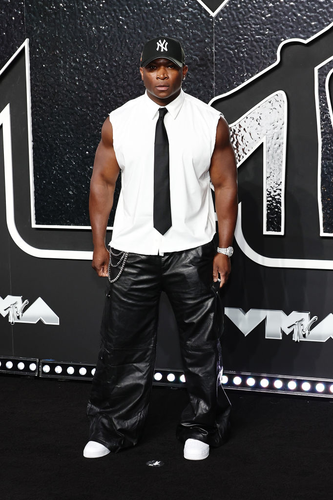 O.T. Genasis on the VMAs red carpet, wearing a sleeveless shirt tie, baggy leather pants, shoes, and a Yankees cap