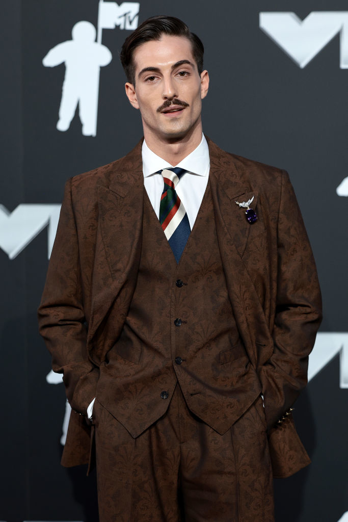Damiano David on the MTV red carpet, wearing a patterned three-piece suit, a striped tie, and a mustache