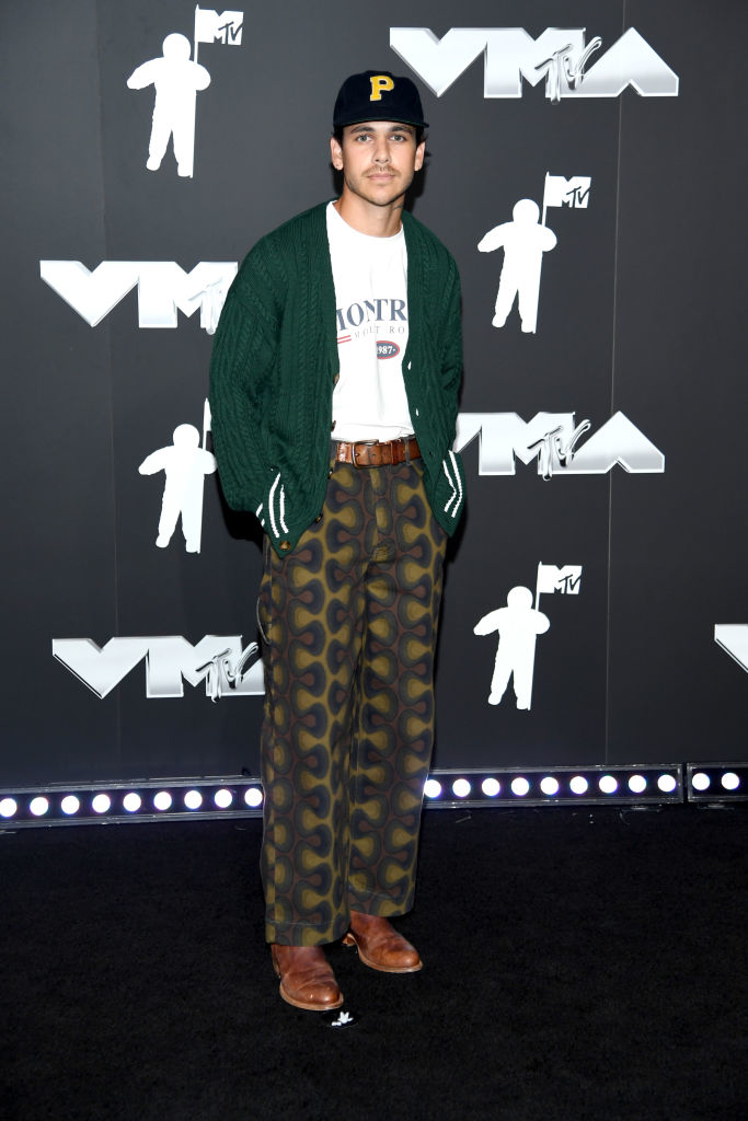 Andrew at the MTV VMA red carpet, wearing a cardigan, t-shirt, patterned pants, and baseball cap