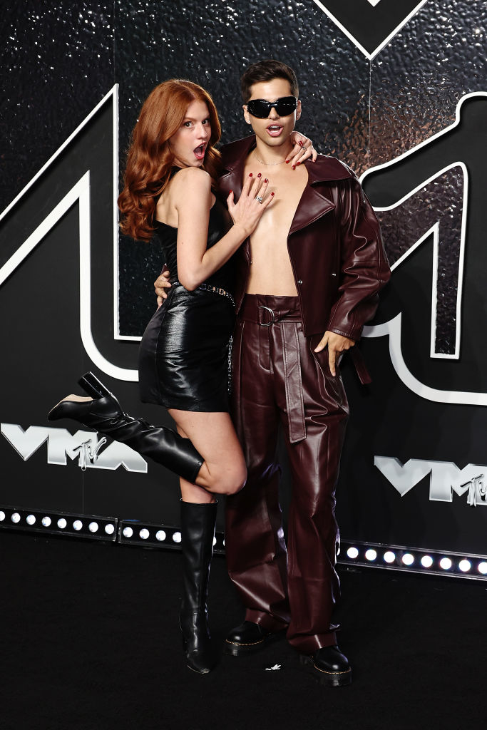 Ashley and Grant on the red carpet at the VMAs. She wears a leather dress and boots, while he sports sunglasses, a leather jacket, and pants
