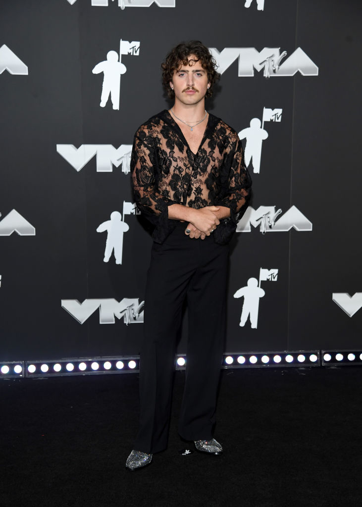 Benson Boone on the VMAs red carpet wearing a sheer lace top and pants, posing for photos
