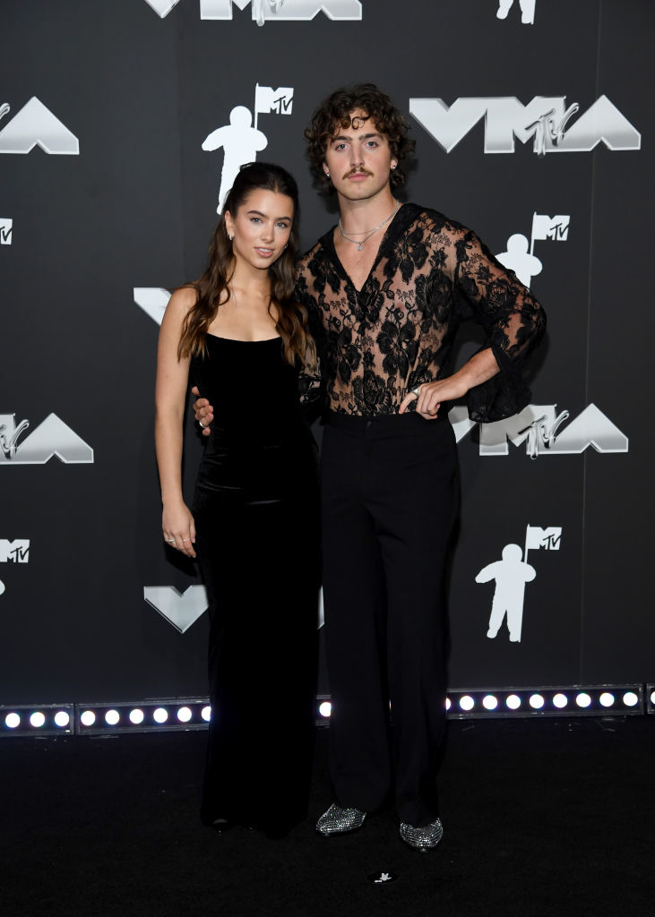 Benson wearing a sheer lace top with dark pants, and Maggie in a sleek gown