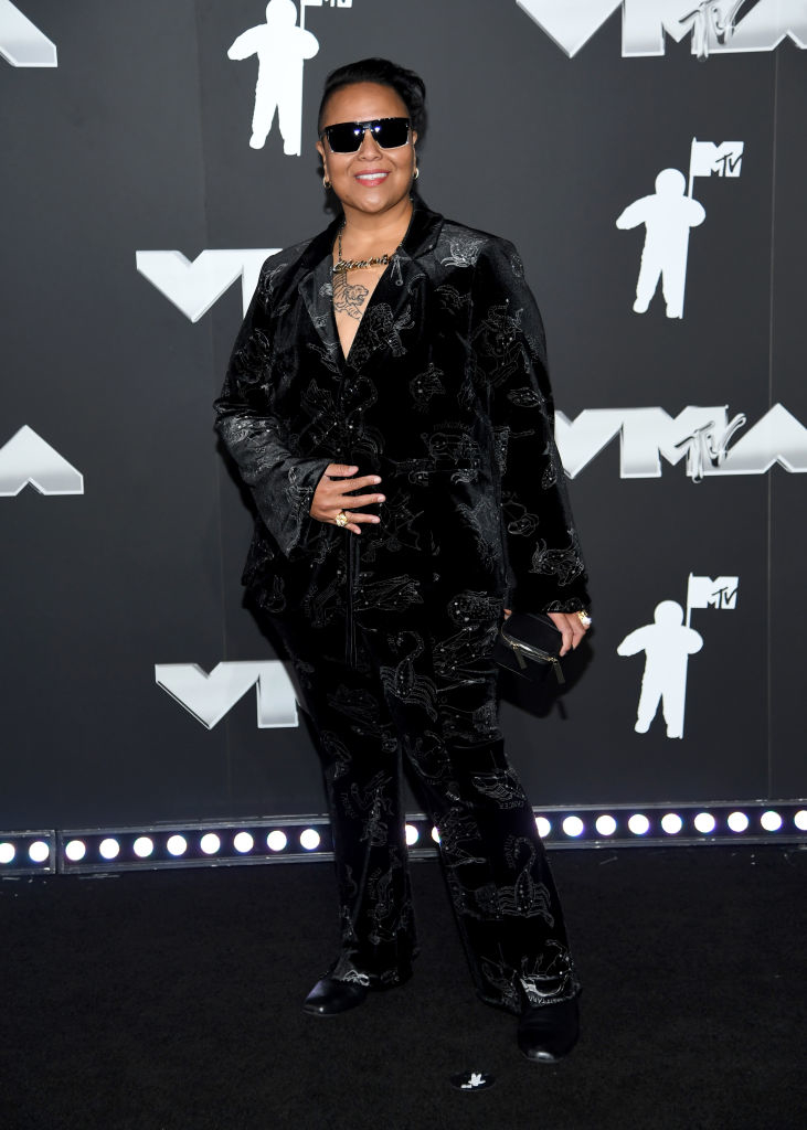 DJ CherishTheLuv is on the red carpet at the MTV VMAs, wearing a stylish velvet suit with intricate patterns and sunglasses