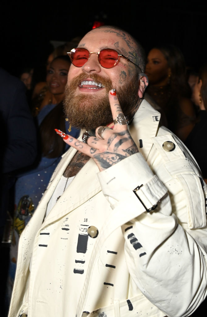 Teddy Swims smiles and makes a rock sign with his hand. His nails are painted and his pinky nail sports a long acrylic