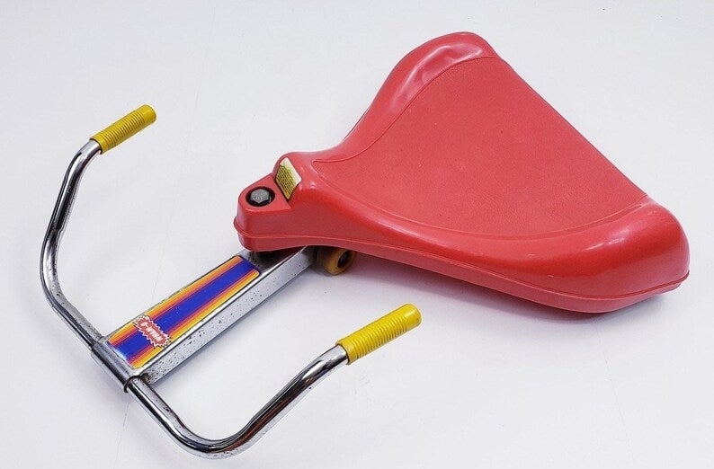 A retro red sit-n-spin toy with yellow handles and a rainbow stripe down the middle, evoking childhood nostalgia