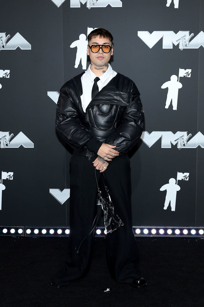 Tiago PZK on the red carpet at the VMAs, wearing a puffy leather jacket, a shirt, dark pants, tie, and oversized sunglasses