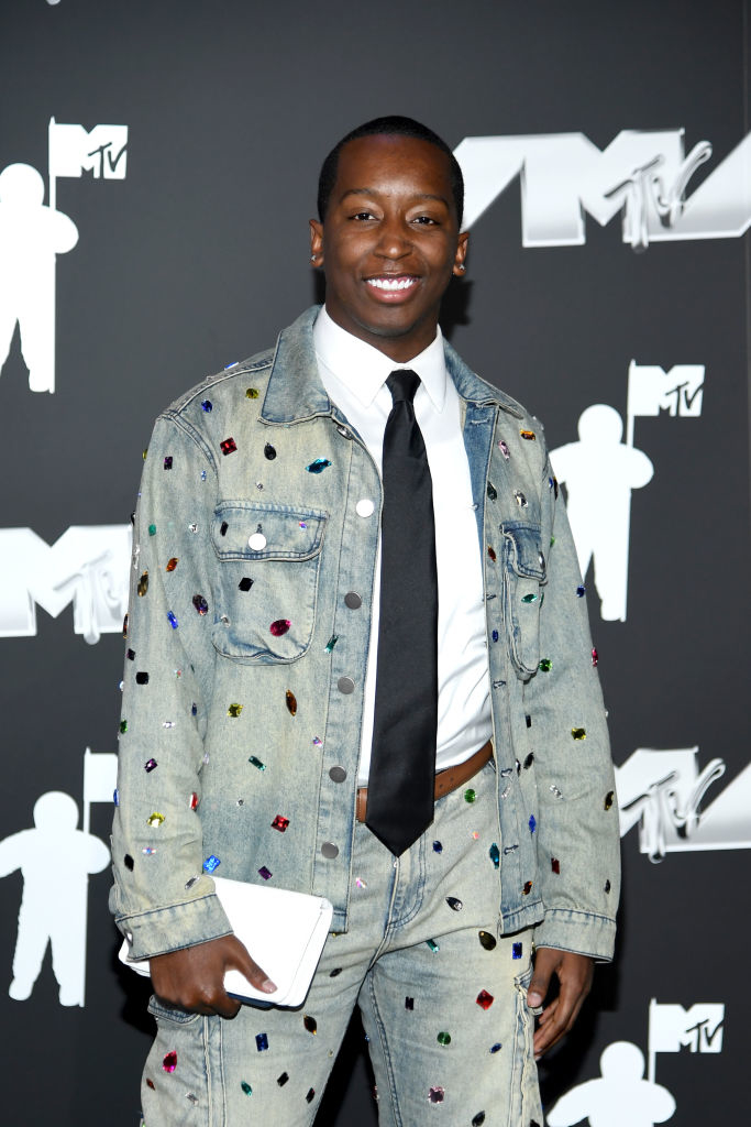 Markell Washington at MTV event wearing a studded and jeweled denim jacket and pants with a shier and tie, holding a clutch